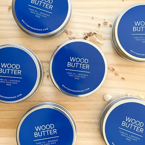 Tin of Wood Butter with blue lids on a wooden surface.