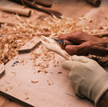 Woodworking scene with hands using a chisel on a wooden surface with wood shavings.