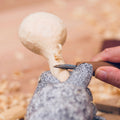 Person carving a mushroom with a knife on a textured surface