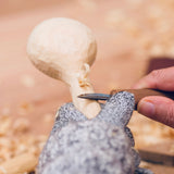 Person carving a mushroom with a knife on a textured surface